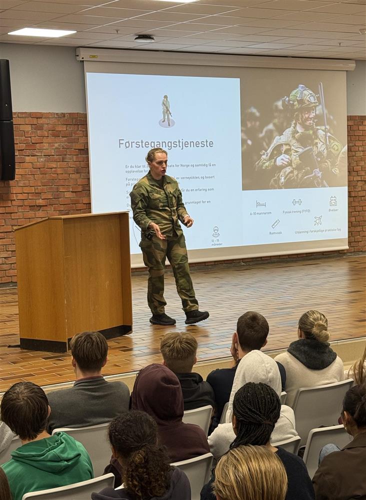 Elever sitter og følger med på representant fra Forsvaret som står å scenen i aula på videregående skole - Klikk for stort bilde