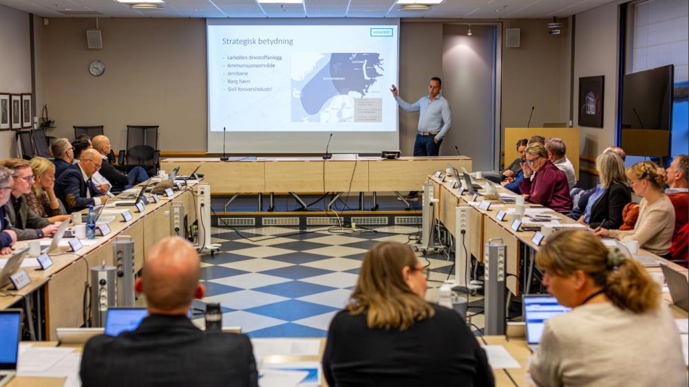 Mennesker på møte, ser på mann som har presentasjon på storskjerm. - Klikk for stort bilde