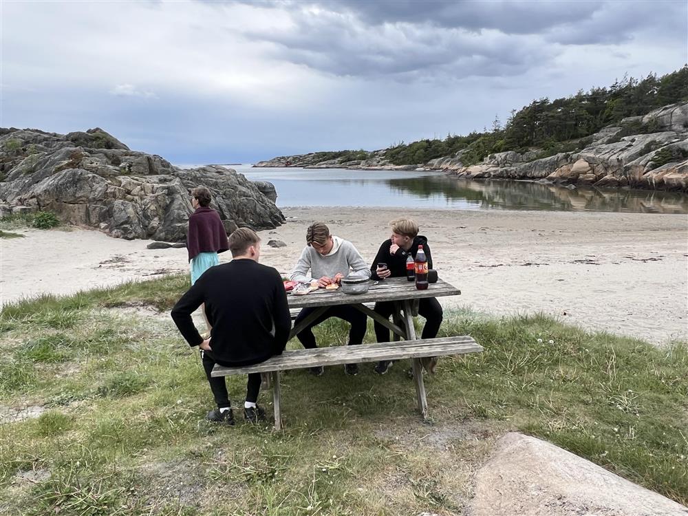Benk ved strandkanten, personer sitter og prater - Klikk for stort bilde