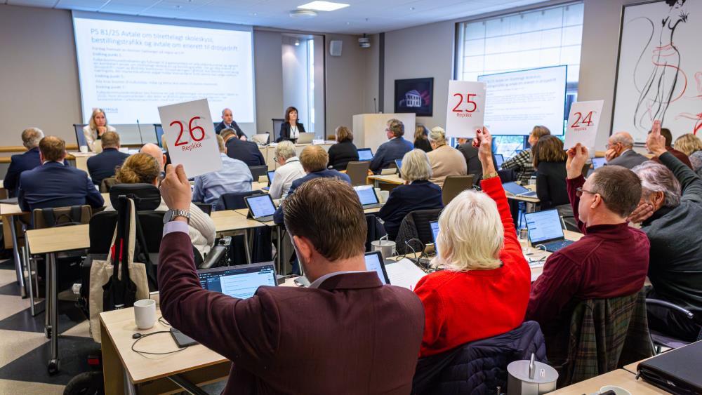 Politikere sitter ved pulter i en sal og stemmer over saker i fylkestinget.  - Klikk for stort bilde